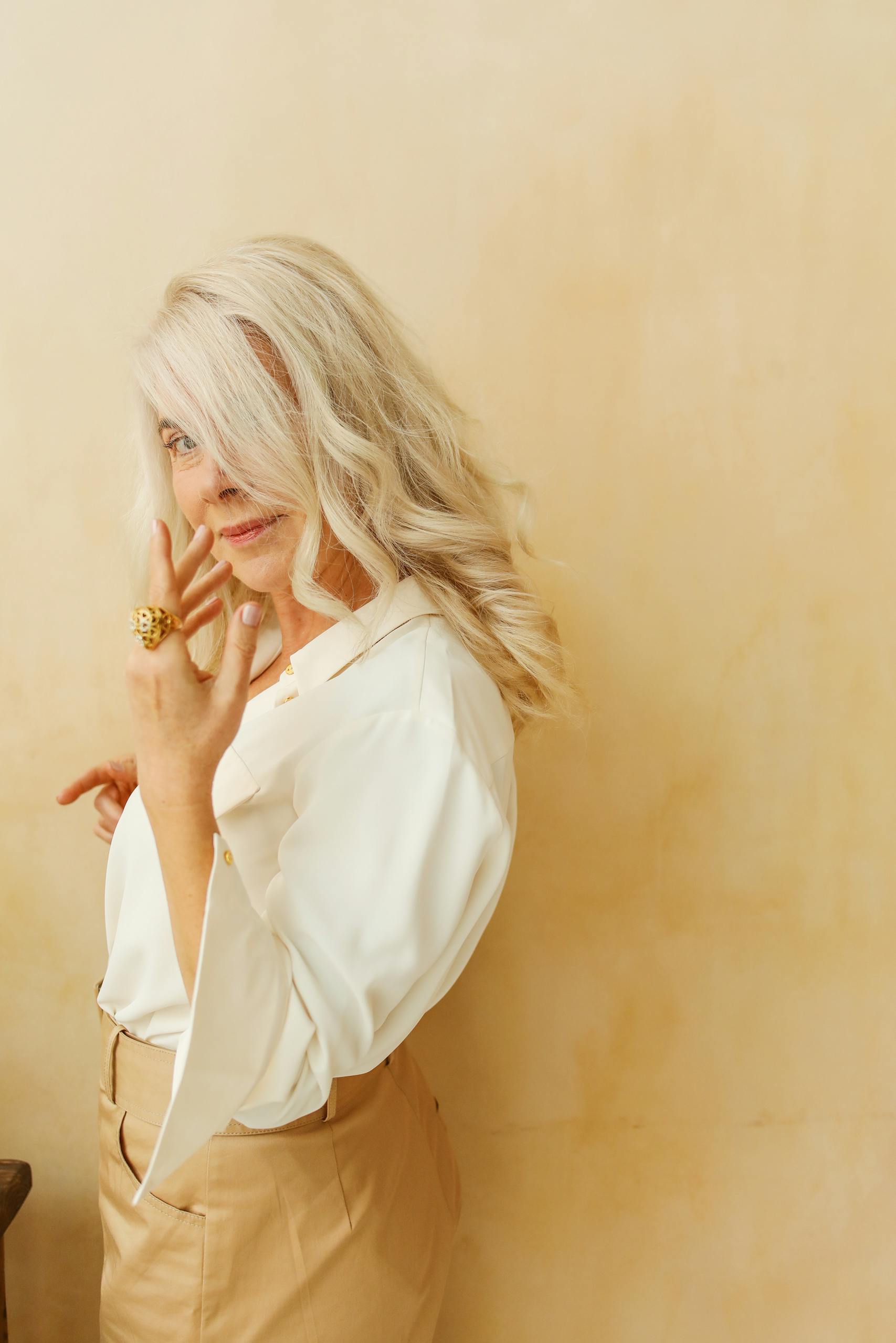 Charming senior woman with white hair poses gracefully against a beige background, exuding confidence.